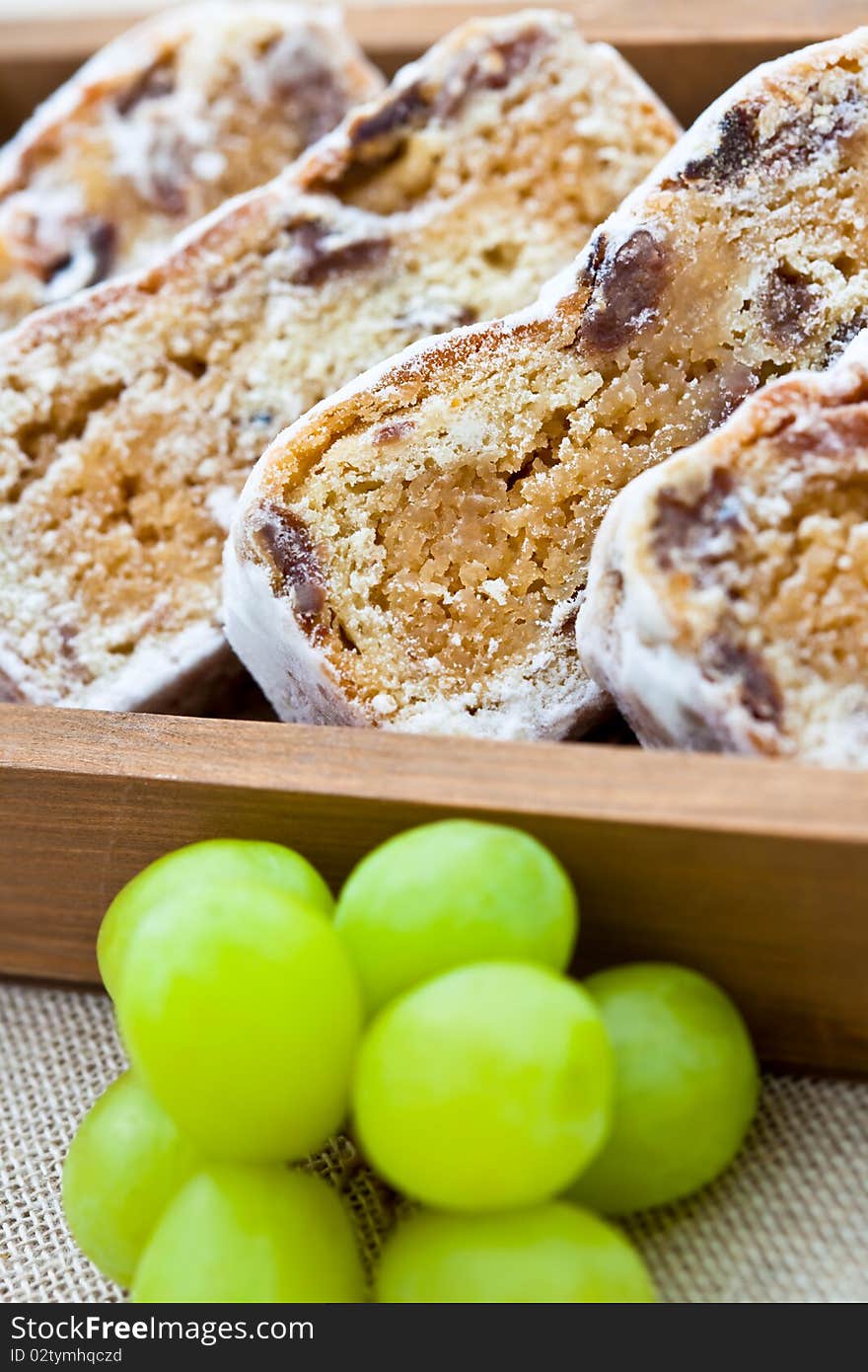 Slices of stollen cake in a wooden box with fresh green grapes. Shallow DOF. Slices of stollen cake in a wooden box with fresh green grapes. Shallow DOF