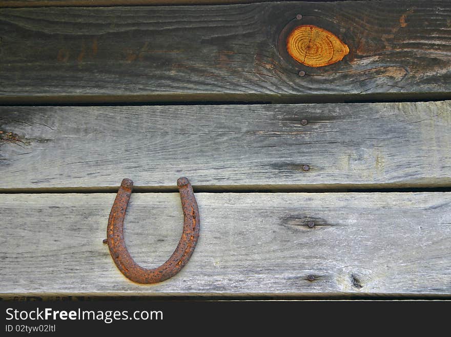 A rusty horseshoe hangs on a barn wall, with a prominent knot in one of the planks. A rusty horseshoe hangs on a barn wall, with a prominent knot in one of the planks