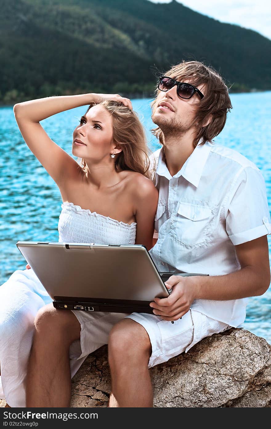 Happy young couple sitting together near the sea with a laptop. Happy young couple sitting together near the sea with a laptop.