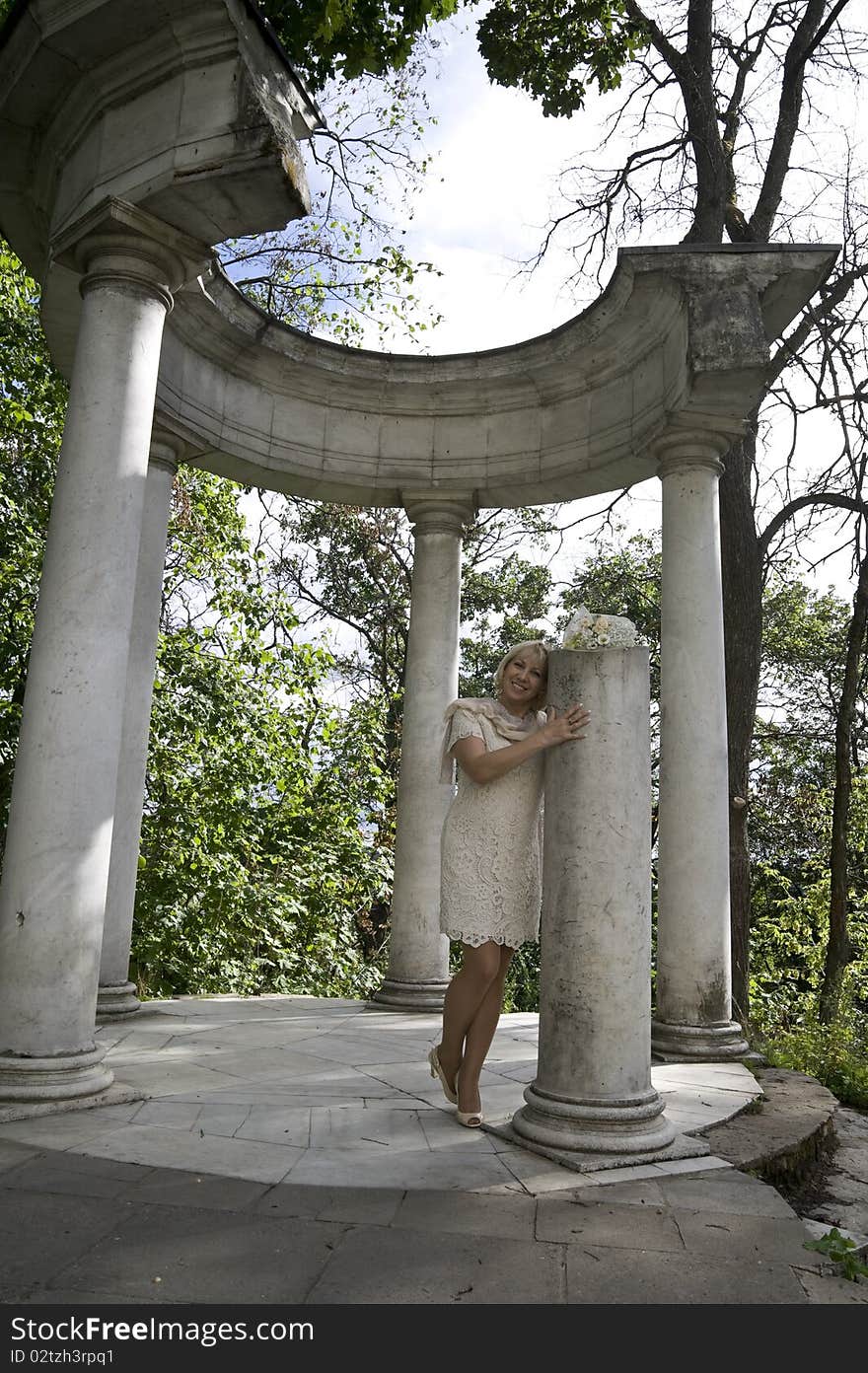 The elegant woman costs at the broken column with a bunch of flowers in an arbor a rotunda. The elegant woman costs at the broken column with a bunch of flowers in an arbor a rotunda