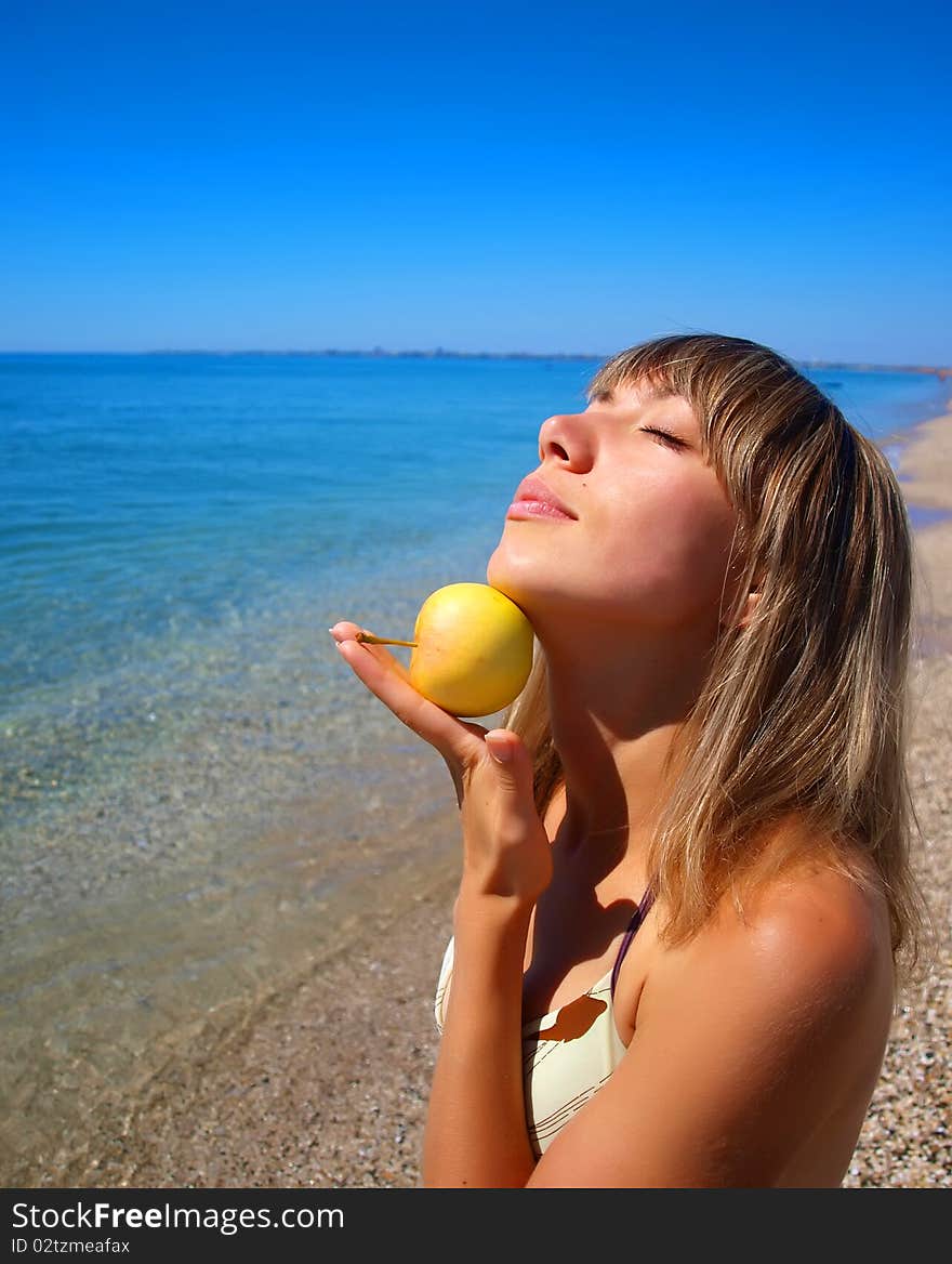 Beautiful young woman with apple on seashore