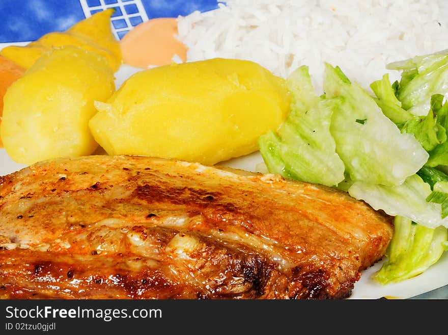 A cutlet with potatoes, salad and rice on a plate