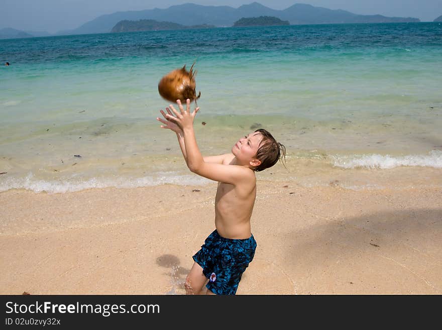 Boy is playing with a coconut on a beach