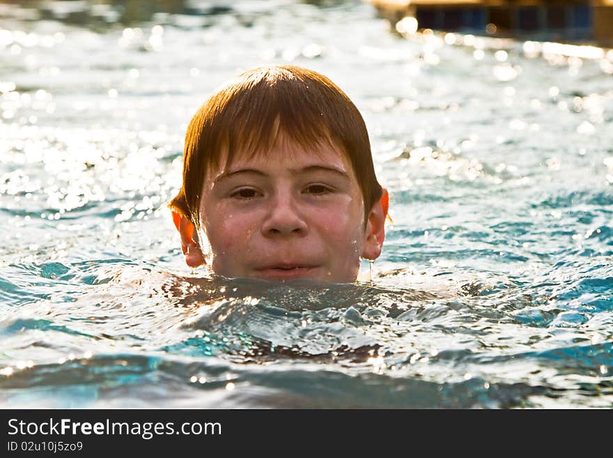 Boy with red hair is swimming in the pool