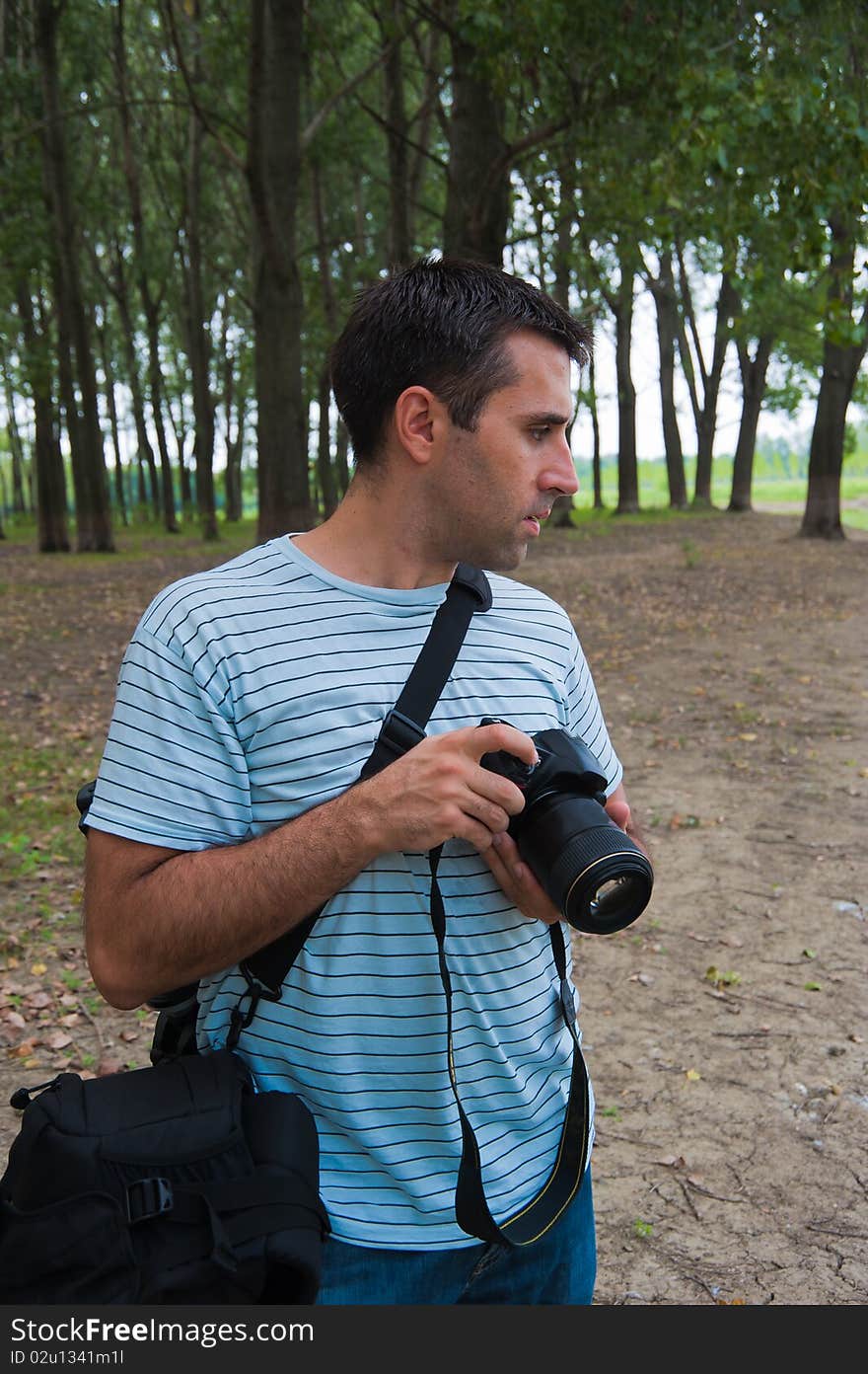 Young photographer looking side-ways, waiting for the photo opportunity outdoors, near a river in woods. Young photographer looking side-ways, waiting for the photo opportunity outdoors, near a river in woods