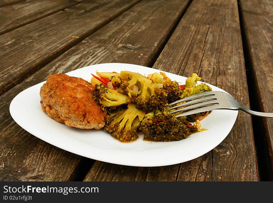 Cutlet and Broccoli in a white plate on wooden table