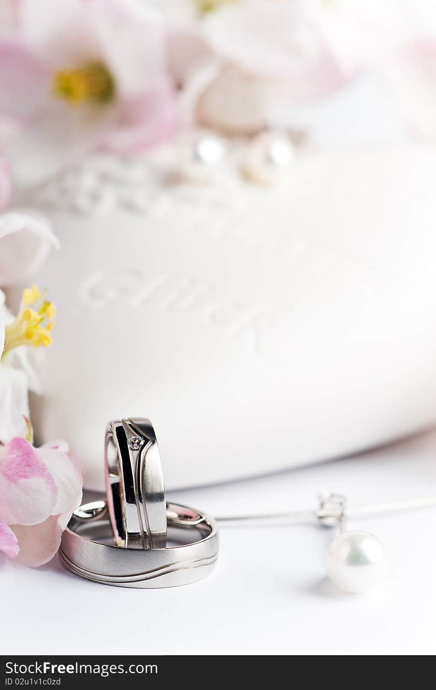 Two wedding rings with earrings and flowers in the background