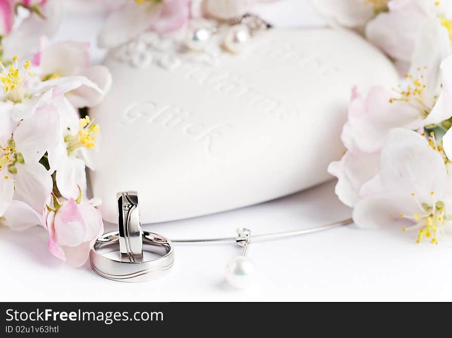 Two wedding rings with earrings and flowers in the background