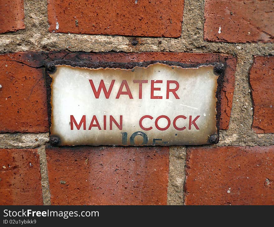 Red brick wall with aged water mains sign that has rusted. Red brick wall with aged water mains sign that has rusted