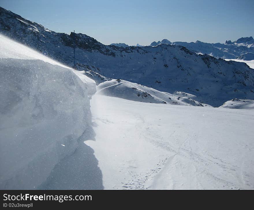 A breeze blowing ice crystals from the top of a snowdrift across a ski run in the French Alps. A breeze blowing ice crystals from the top of a snowdrift across a ski run in the French Alps.