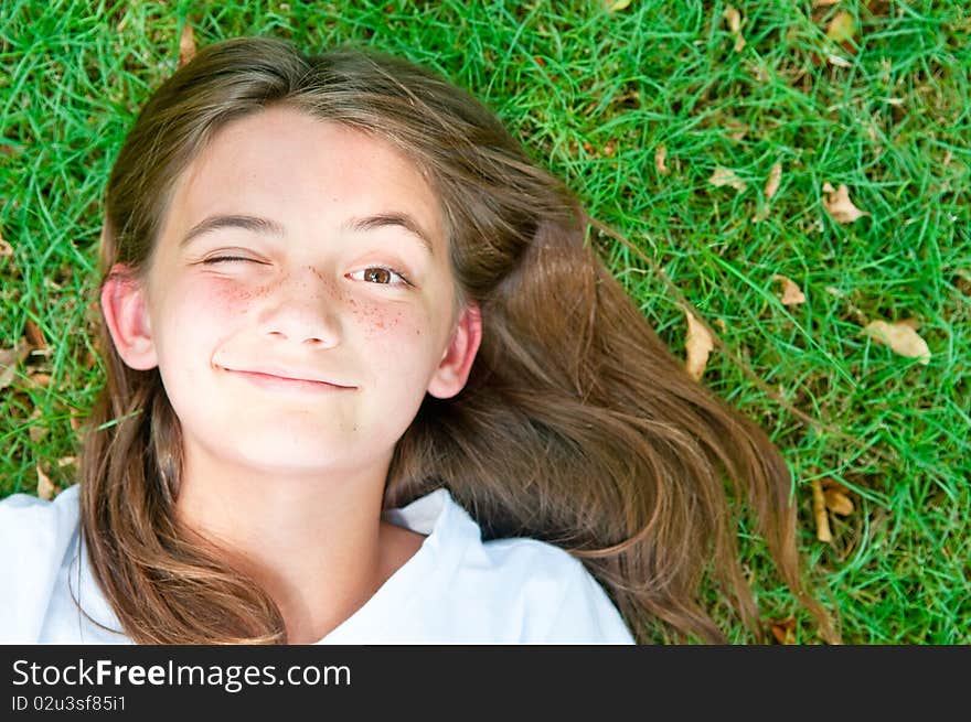 A happy young girl resting on the grass winks at the camera. A happy young girl resting on the grass winks at the camera