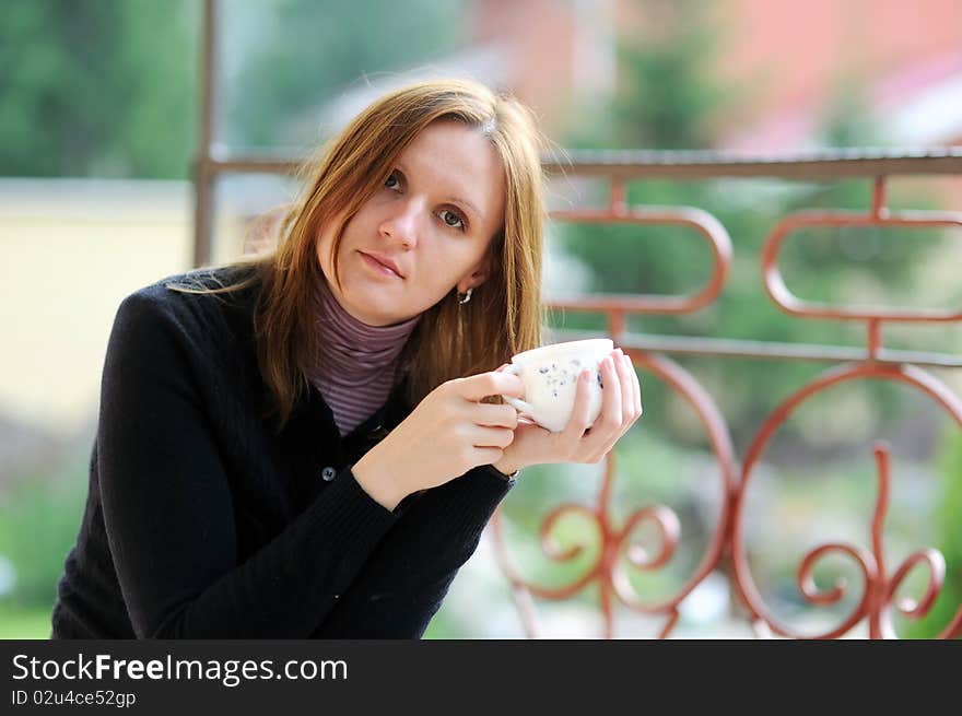 Young woman with cup in her hand on the balcony in the autumn