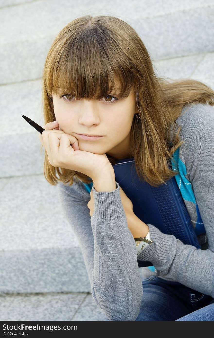 Schoolgirl sitting on the stairs with a notebook and pen. Thinking