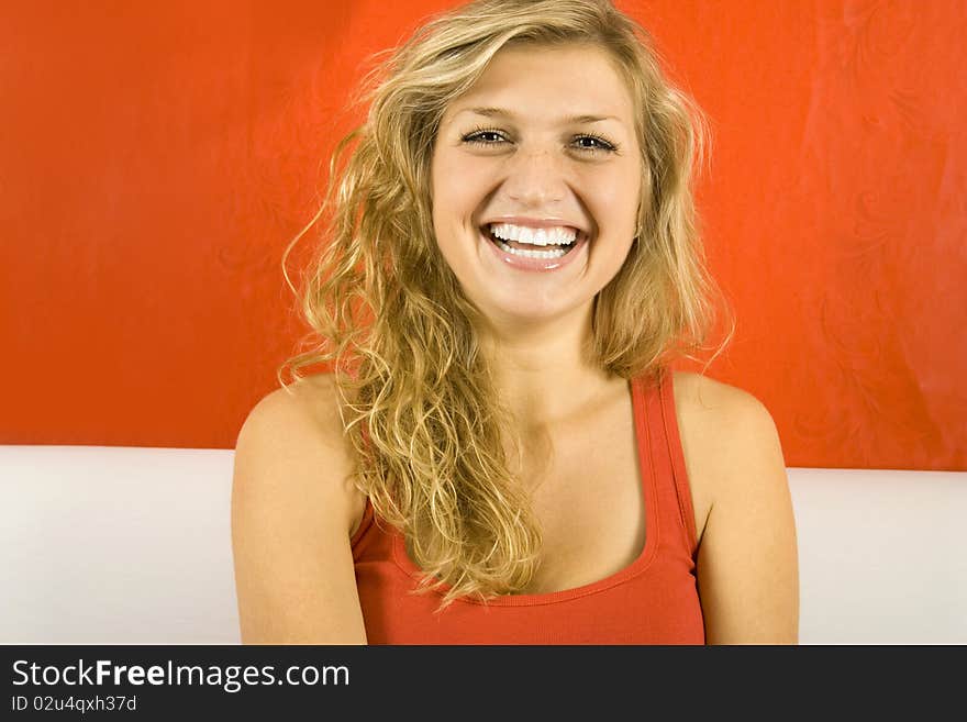 Young beautiful woman against the red wall is sitting on the sofa and laughs. Young beautiful woman against the red wall is sitting on the sofa and laughs