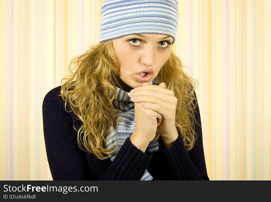 Photo of a young woman in a blue sweater with a blue knit cap and scarf. She breathes on his hands to warm them. Photo of a young woman in a blue sweater with a blue knit cap and scarf. She breathes on his hands to warm them