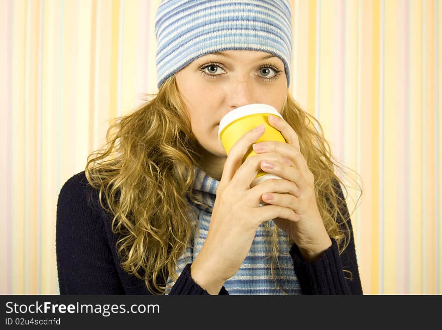 Photo of a young woman in a blue sweater with a blue knit cap and scarf. Girl drinks coffee from a paper cup. Photo of a young woman in a blue sweater with a blue knit cap and scarf. Girl drinks coffee from a paper cup