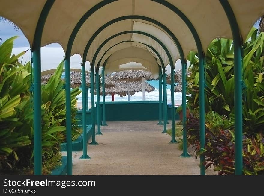 Resort covered walkway with vegetation on each side and beach huts in the background