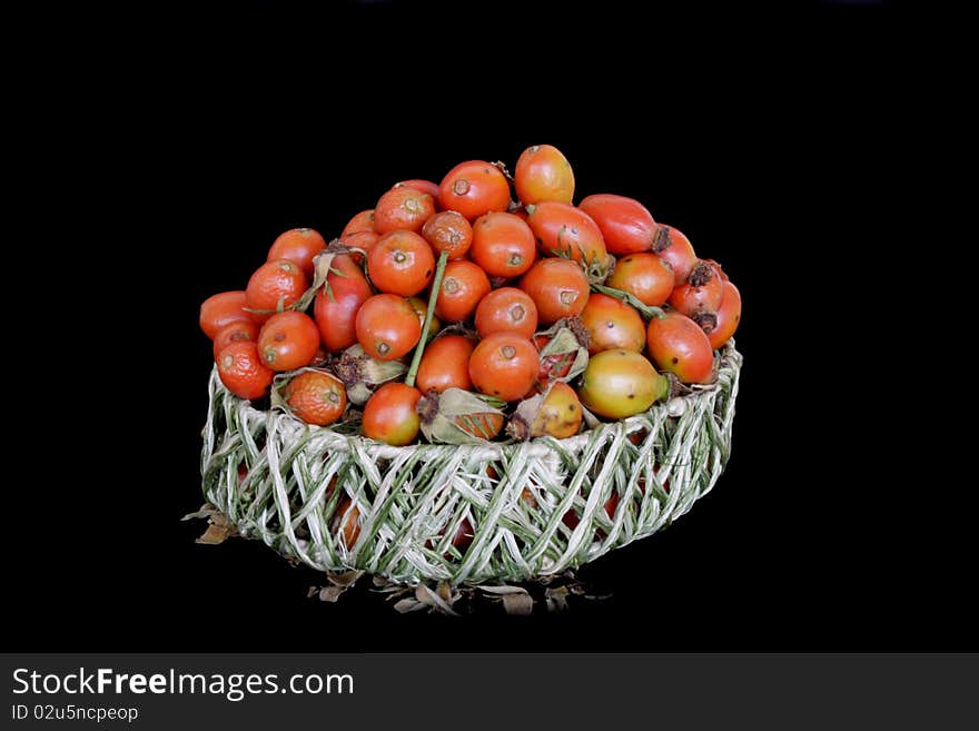 Ripe berries of dog-rose in wicker basket in isolated over black