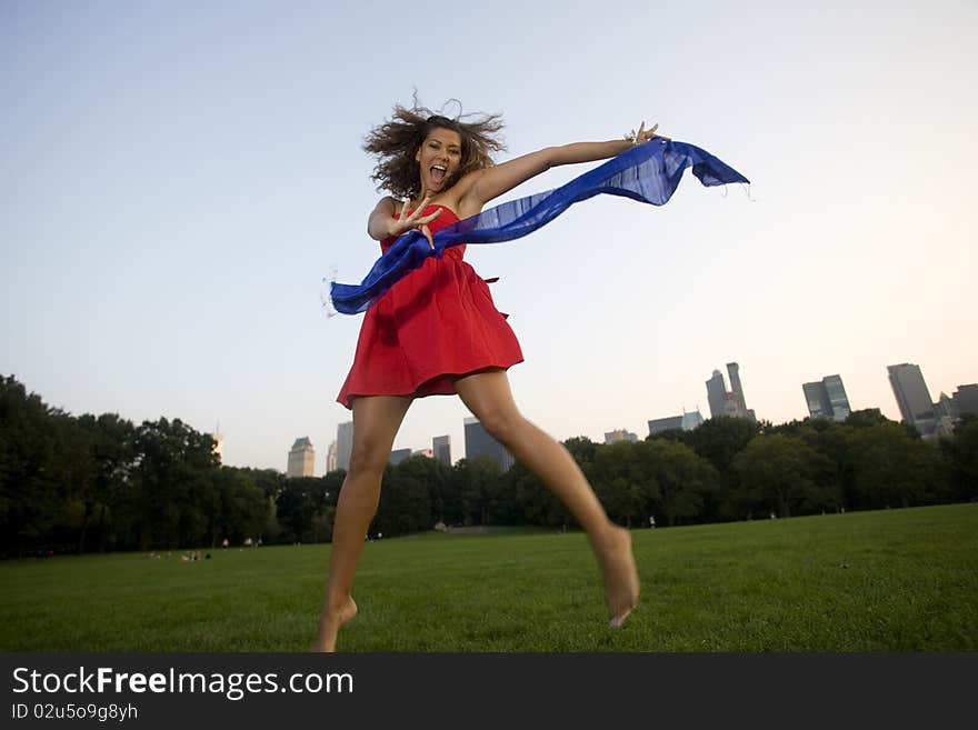 A happy woman wearing red with a blue scarf jumps for joy in a city park. A happy woman wearing red with a blue scarf jumps for joy in a city park