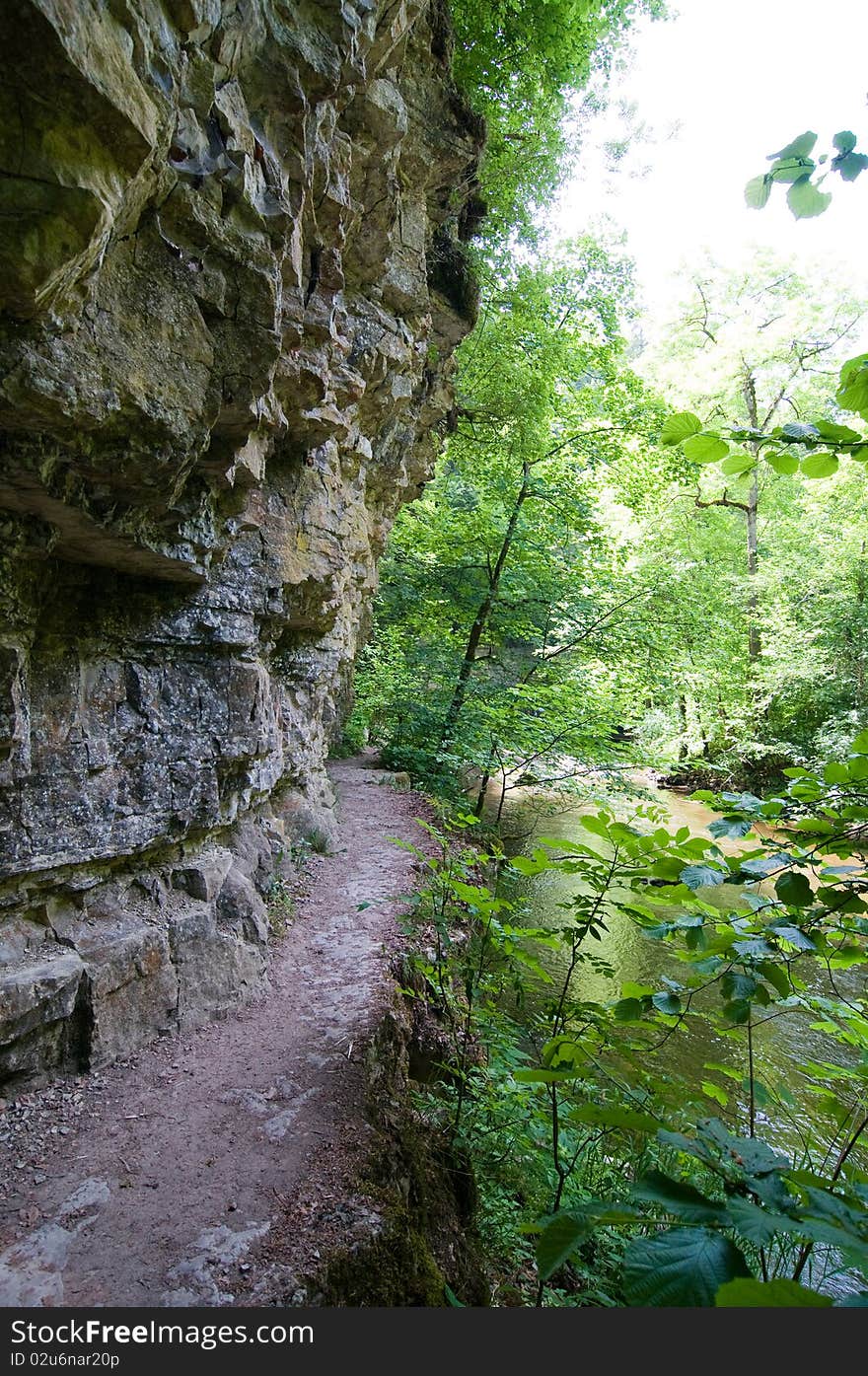 Hiking trail between cliff, rocks and river