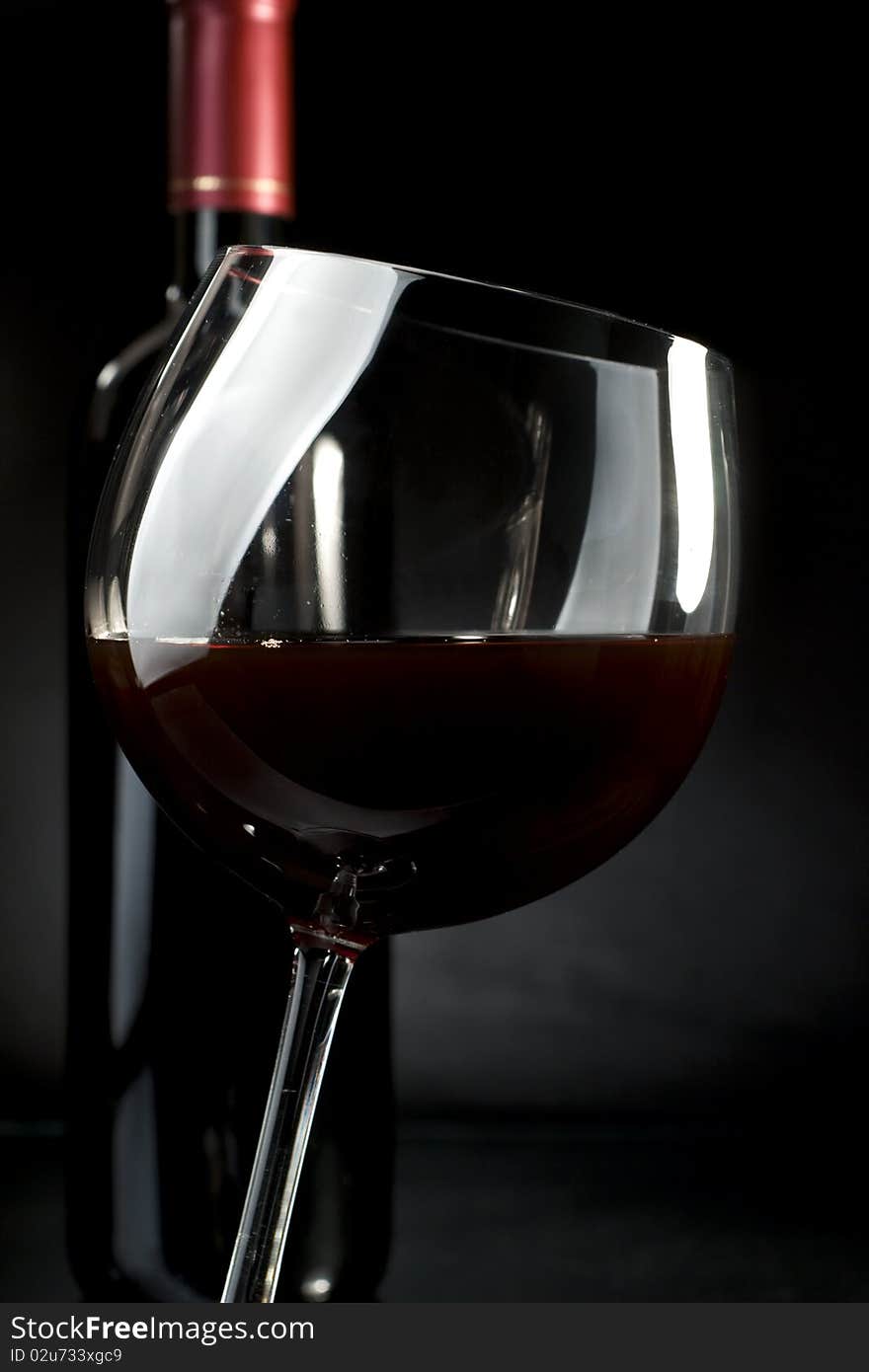 Bottle and glass of red wine on a dark background