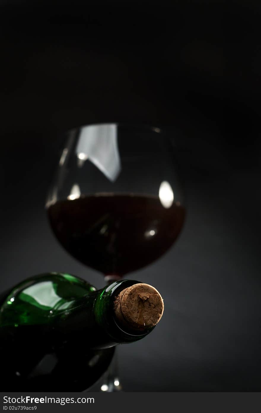 Bottle and glass of red wine on a dark background