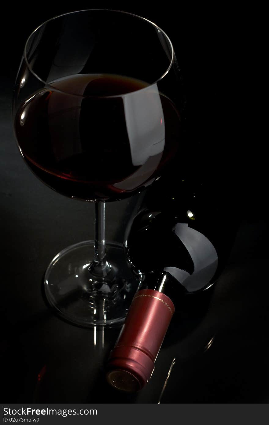 Bottle and glass of red wine on a dark background