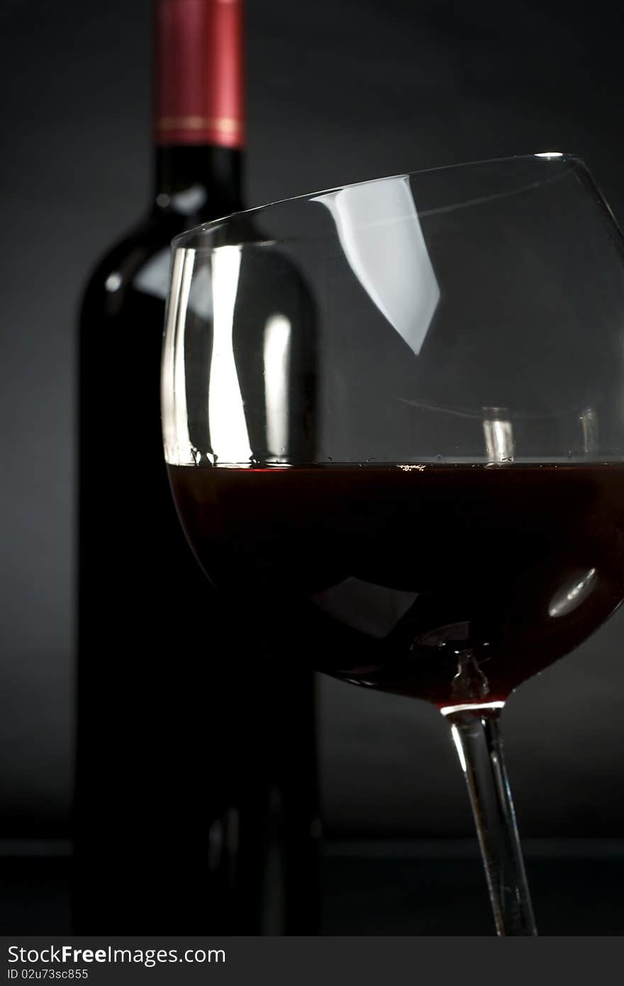 Bottle and glass of red wine on a dark background