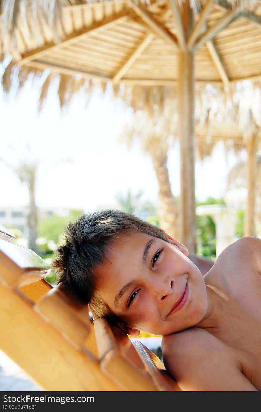 Smiling teenage boy portrait lying under sunshade on beach. Smiling teenage boy portrait lying under sunshade on beach