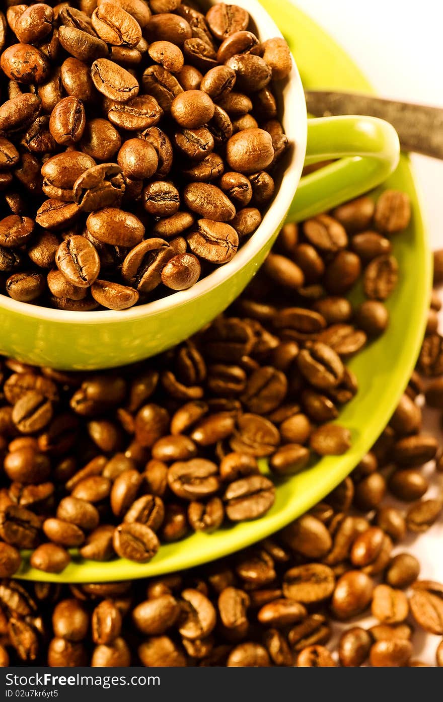 Green cup of coffee with brown beans on white ground