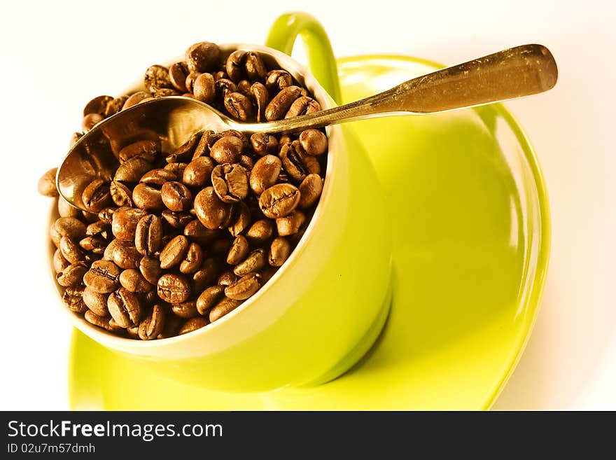 Green cup of coffee with brown beans on white ground