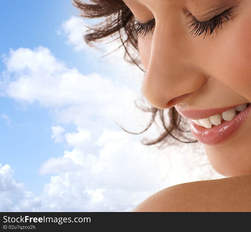 Portrait of a young and happy brunette girl. The image is taken on a cloudy background.