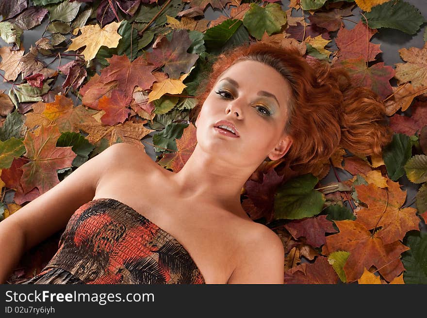 Autumn image with a beautiful girl in a vivid dress lying in fallen leaves. Autumn image with a beautiful girl in a vivid dress lying in fallen leaves.