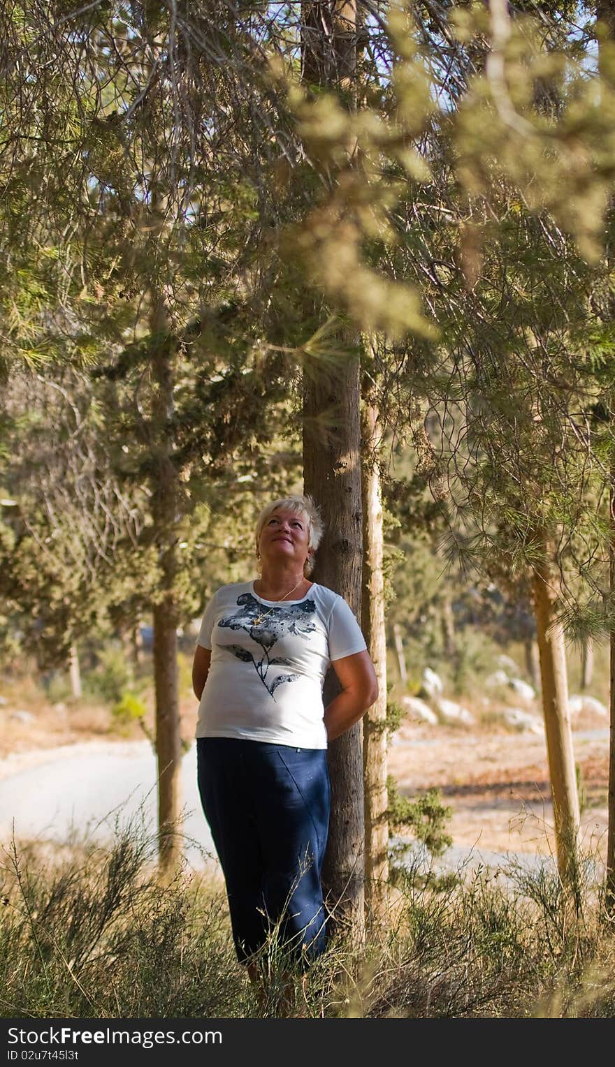 Casual portrait of happy mature woman against a background of pine trees. Casual portrait of happy mature woman against a background of pine trees.