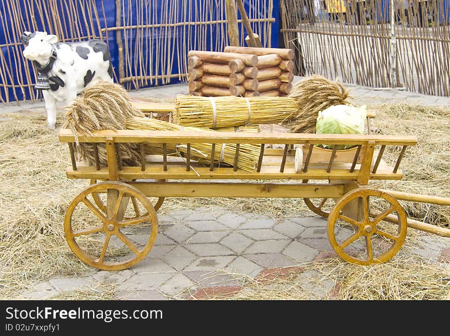 The cart with collected wheat and cabbage costs near a wattle fence. The cart with collected wheat and cabbage costs near a wattle fence