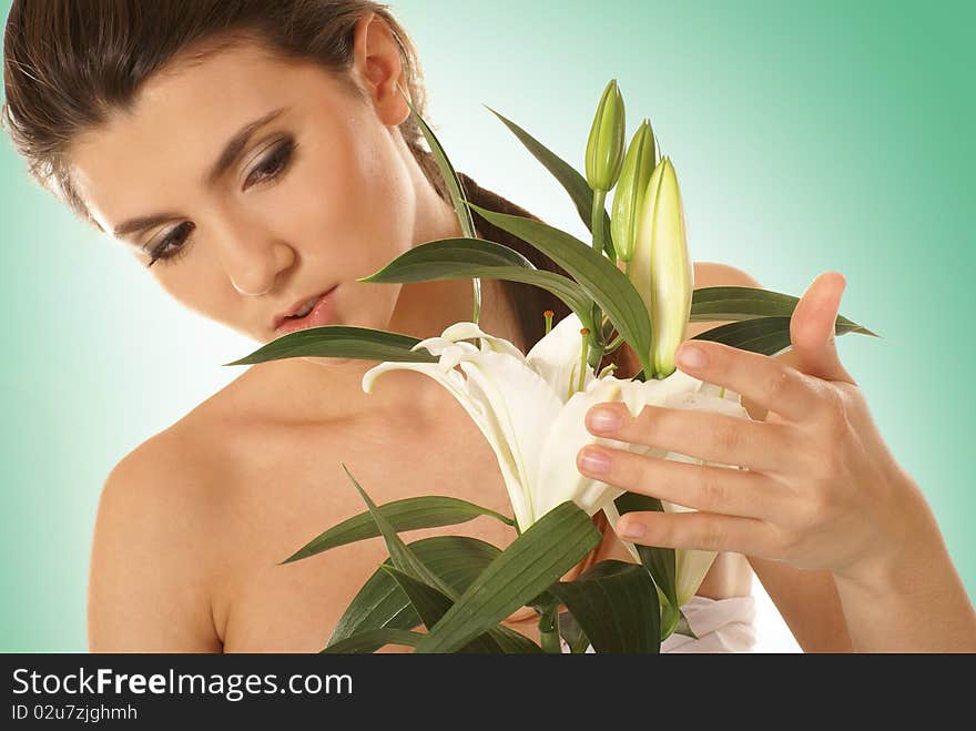 A young and attractive brunette woman with a beautiful lily flower. The image is isolated on a light green gradient background. A young and attractive brunette woman with a beautiful lily flower. The image is isolated on a light green gradient background.