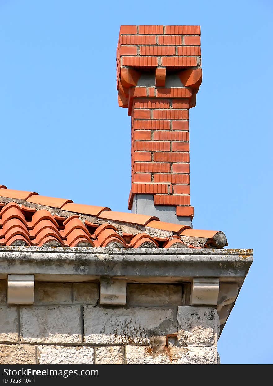 Closeup of the old tiled roof and new red chimney on the blue sky.