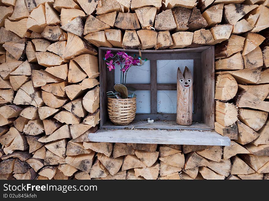 Wooden window with orchid in a pot and wooden cat among stock of wooden logs. Wooden window with orchid in a pot and wooden cat among stock of wooden logs.