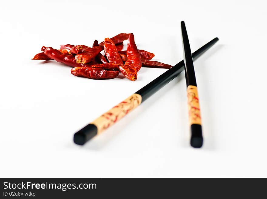 Two chop sticks and some chili fruits on a white background