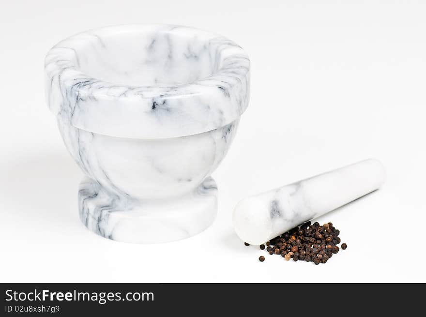 A marble mortar with pestle with some dried black pepper. A marble mortar with pestle with some dried black pepper