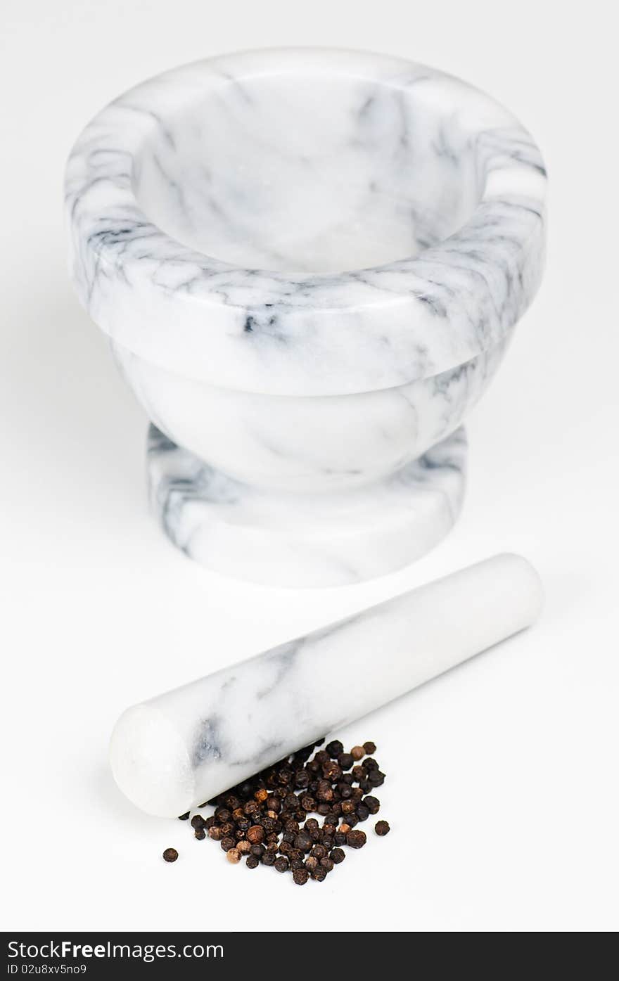 A marble mortar with pestle with some dried black pepper. A marble mortar with pestle with some dried black pepper