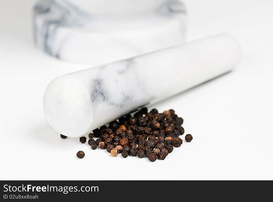 A marble mortar with pestle next to some dried black pepper. A marble mortar with pestle next to some dried black pepper