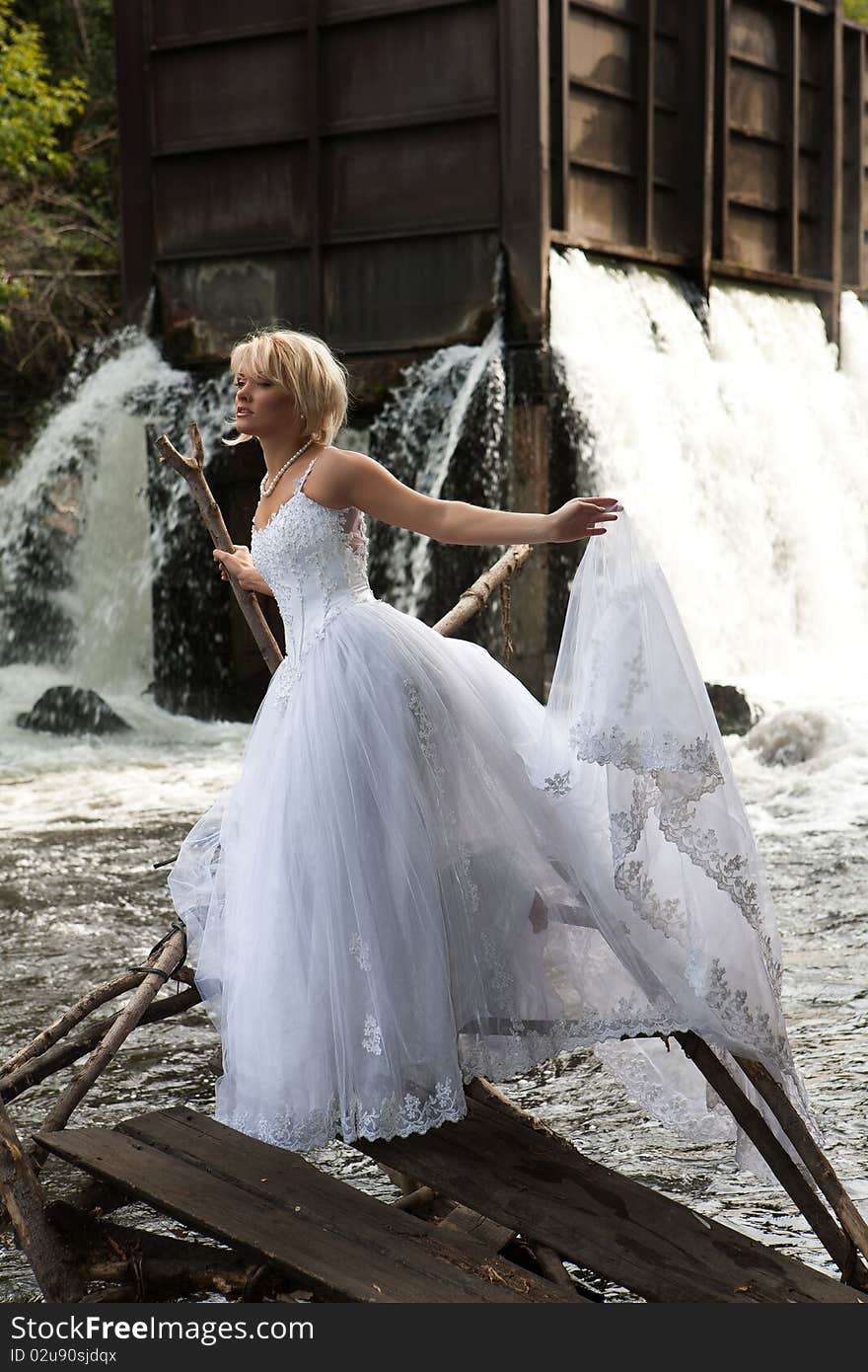 Young blonde woman in a white wedding dress near the waterfall. Young blonde woman in a white wedding dress near the waterfall