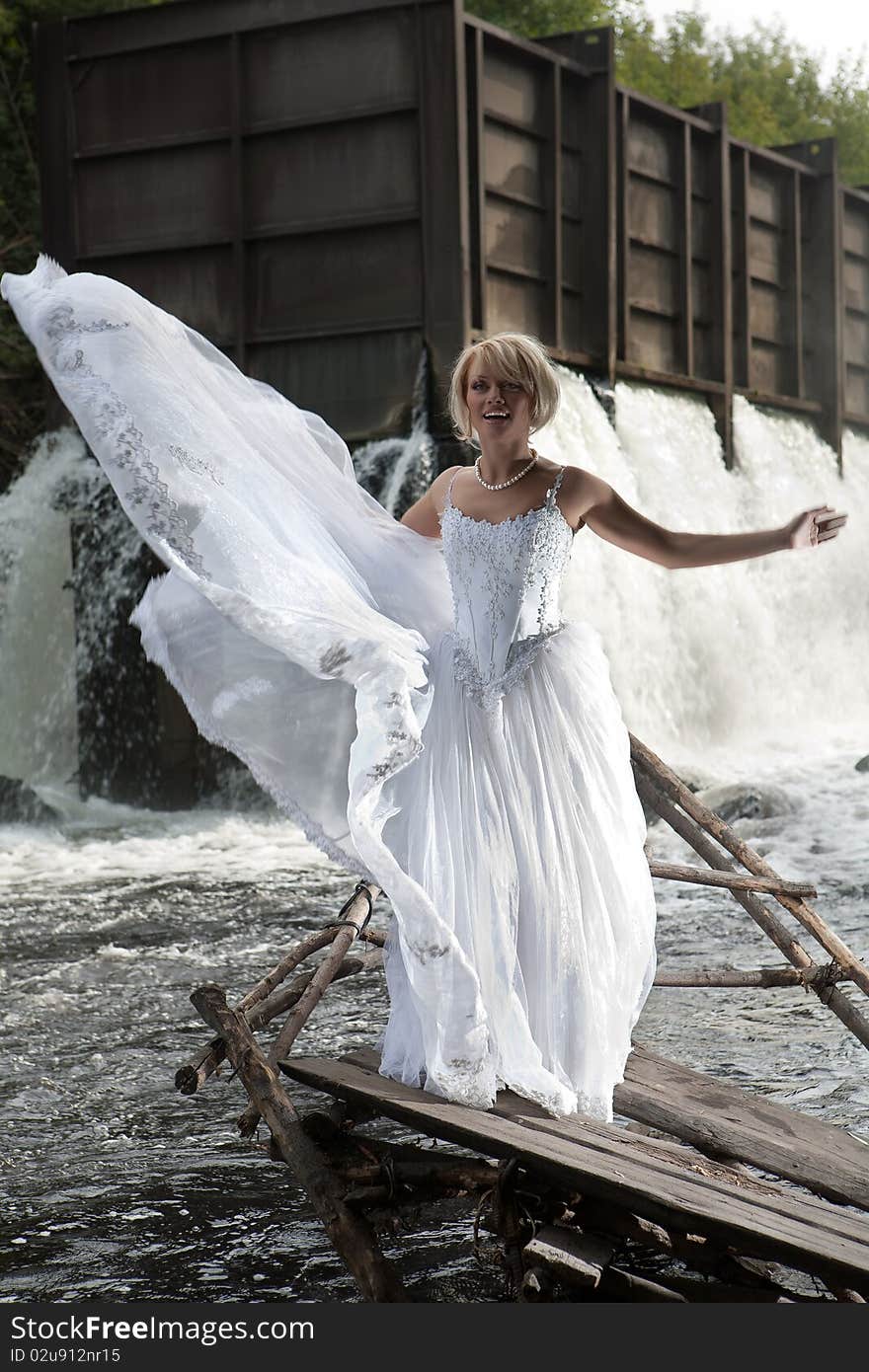 Young blonde woman in a white wedding dress near the waterfall. Young blonde woman in a white wedding dress near the waterfall