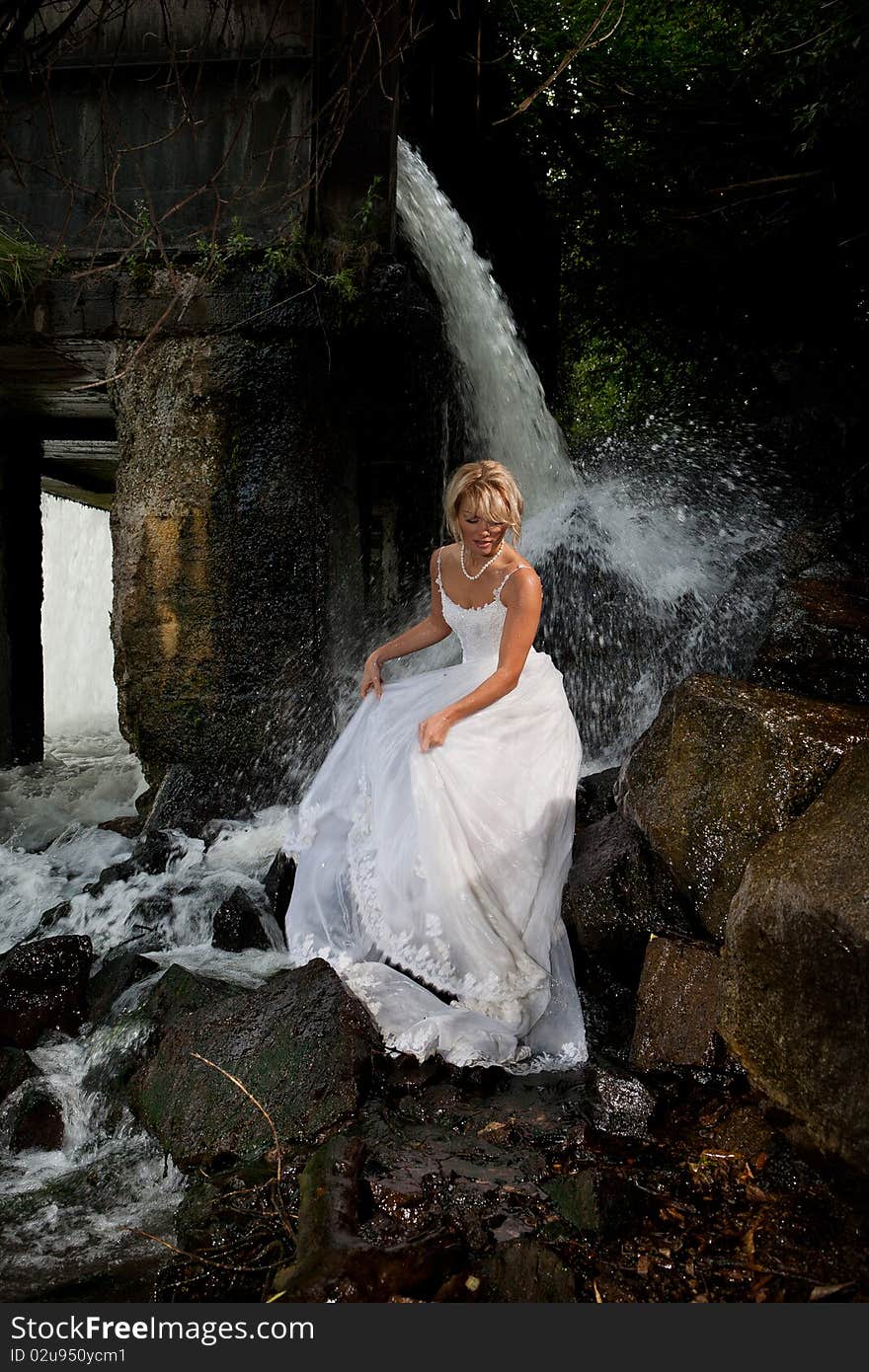 Young blonde woman in a white wedding dress near the waterfall. Young blonde woman in a white wedding dress near the waterfall