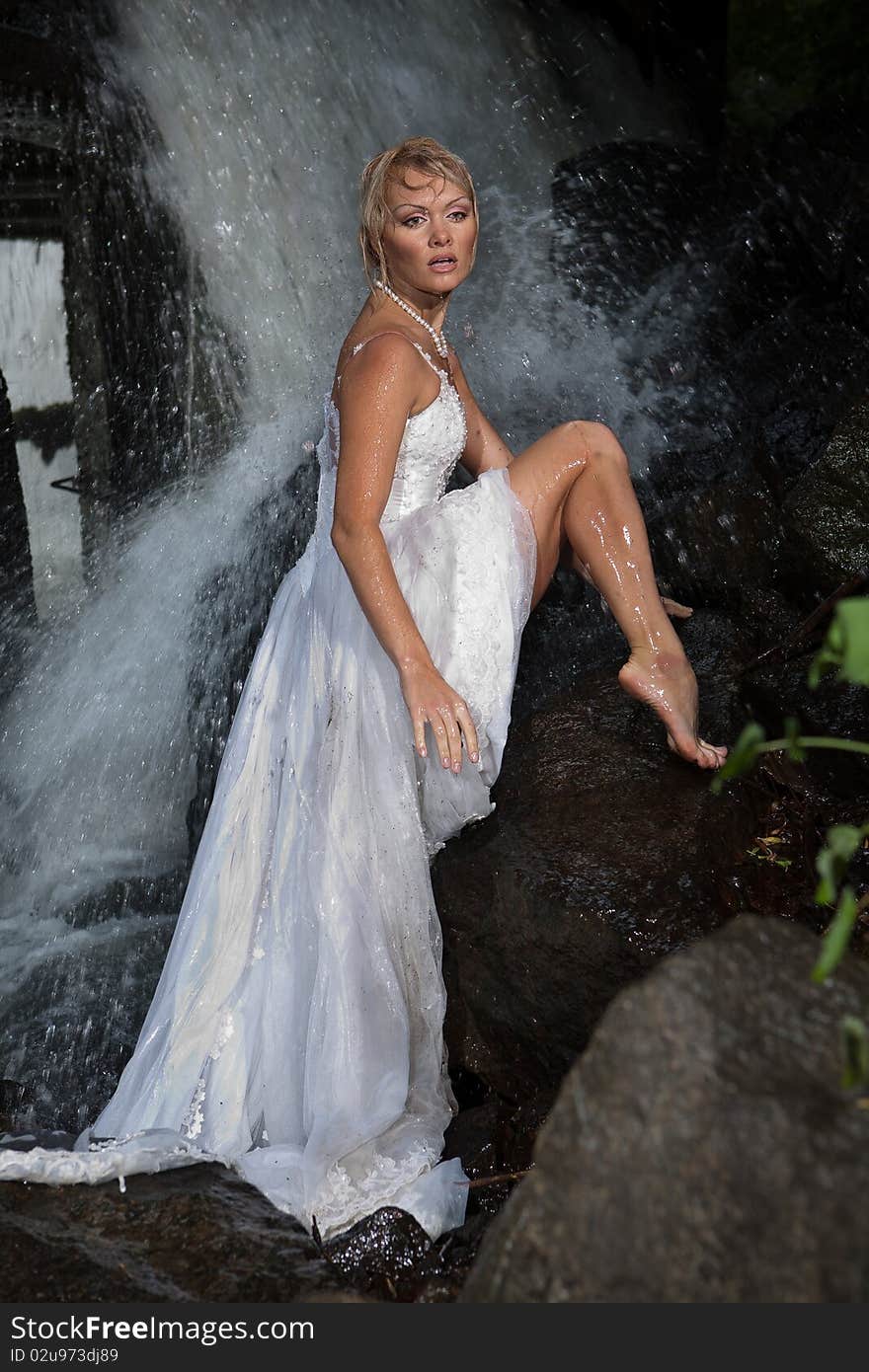 Young blonde woman in a white wedding dress near the waterfall. Young blonde woman in a white wedding dress near the waterfall