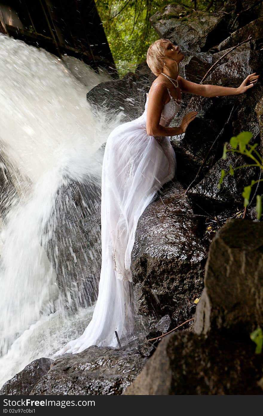 Young blonde woman in a white wedding dress near the waterfall. Young blonde woman in a white wedding dress near the waterfall