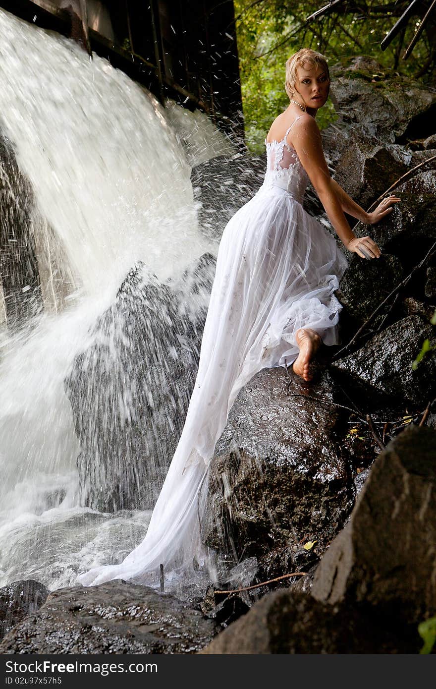 Young blonde woman in a white wedding dress near the waterfall. Young blonde woman in a white wedding dress near the waterfall