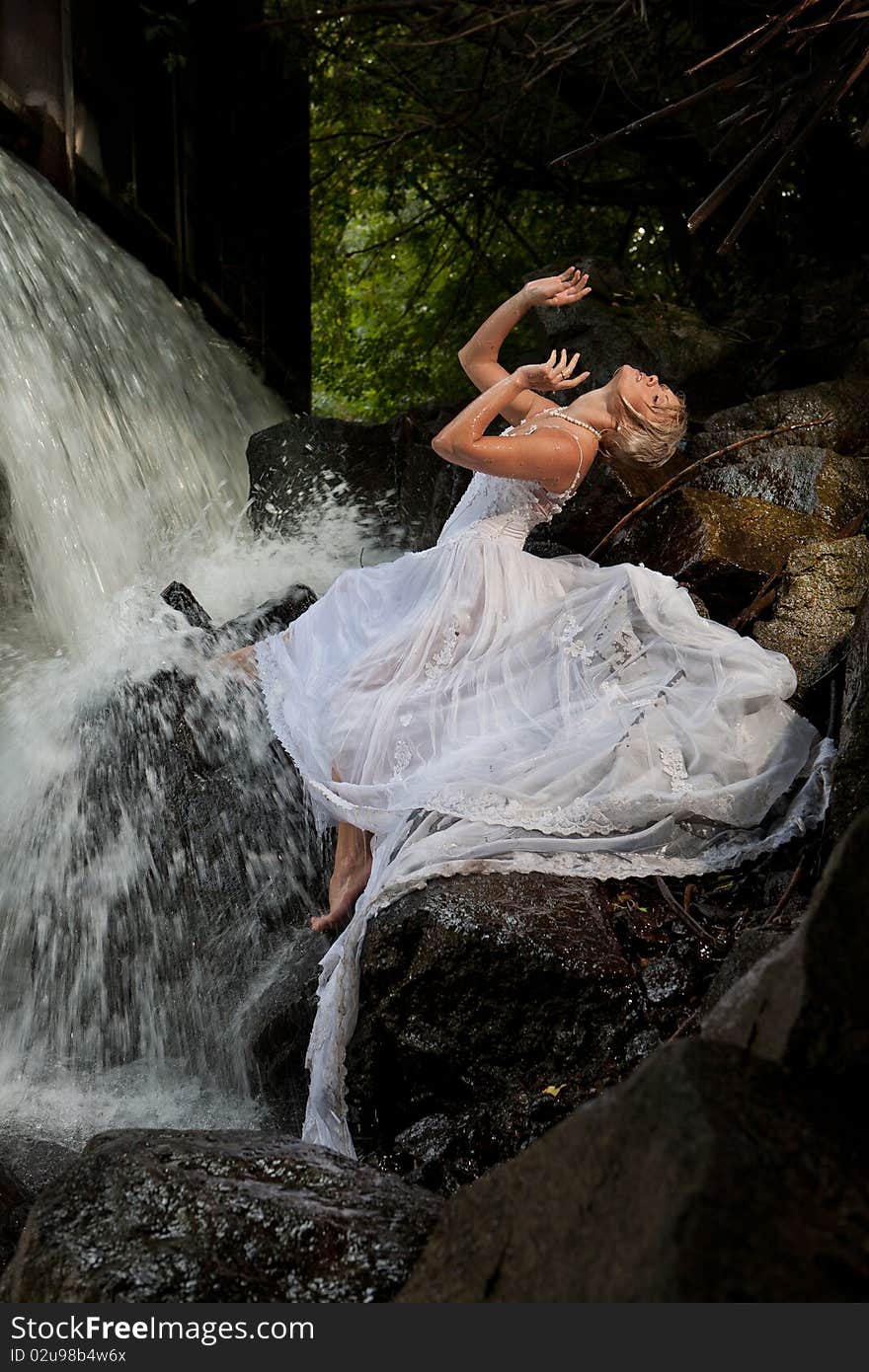 Young blonde woman in a white wedding dress near the waterfall. Young blonde woman in a white wedding dress near the waterfall