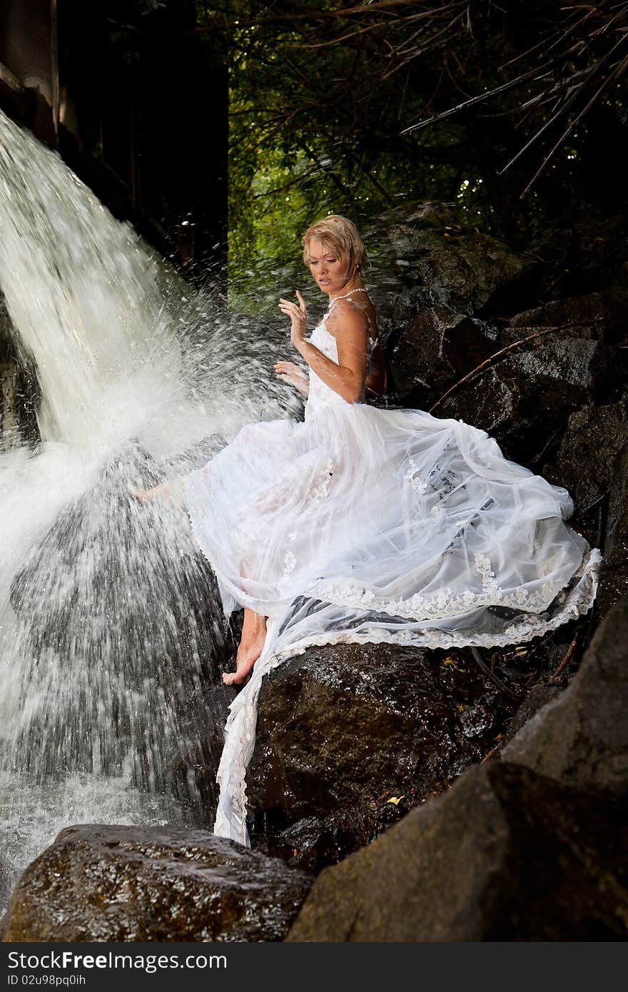 Young blonde woman in a white wedding dress near the waterfall. Young blonde woman in a white wedding dress near the waterfall